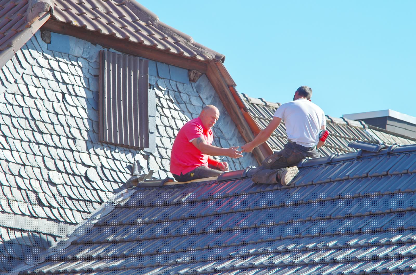 Zwei Dachdecker bei der Arbeit auf einem Steildach mit Gaube